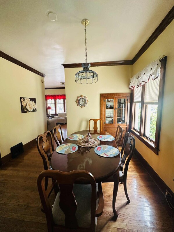 A dining room with a wooden table, chairs, a chandelier, and a view of the outdoors through a window. - Sunday - Sunday Rent in Summer! (Grand Haven)