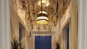 Un couloir avec une porte bleue, des plantes suspendues, un tapis tissé et un luminaire suspendu.