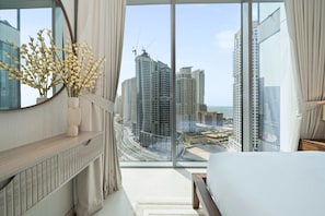 A modern hotel room with a large window, a bed, a bedside table, and a vase of flowers. - Experience 2BR Luxury Living at in LIV Marina (Dubai)