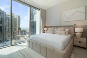 A modern hotel room with a large bed, two bedside tables, a view of tall buildings, and a cityscape. - Experience 2BR Luxury Living at in LIV Marina (Dubai)
