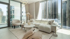 Ein modernes Wohnzimmer mit Sofa, Sessel und Couchtisch, großen Fenstern mit Blick auf die Stadt und einer Kristallleuchter.