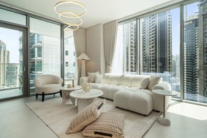 A modern living room with a sofa, armchair, and coffee table, large windows with city views, and a chandelier. - Experience 2BR Luxury Living at in LIV Marina (Dubai)