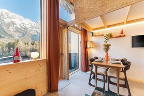 Una stanza accogliente con arredamento in legno, un tavolo da pranzo apparecchiato per due persone e vista sulle montagne innevate.