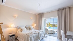 Ein Schlafzimmer mit Bett, Nachttischen, einem Schreibtisch und Blick auf einen Pool.