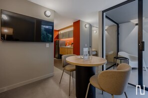 A modern hotel room with a round dining table, two chairs, a flat-screen TV, and a kitchen area visible through an open door. - NOK Luxury 3BR in Zona Rosa (Bogotá)