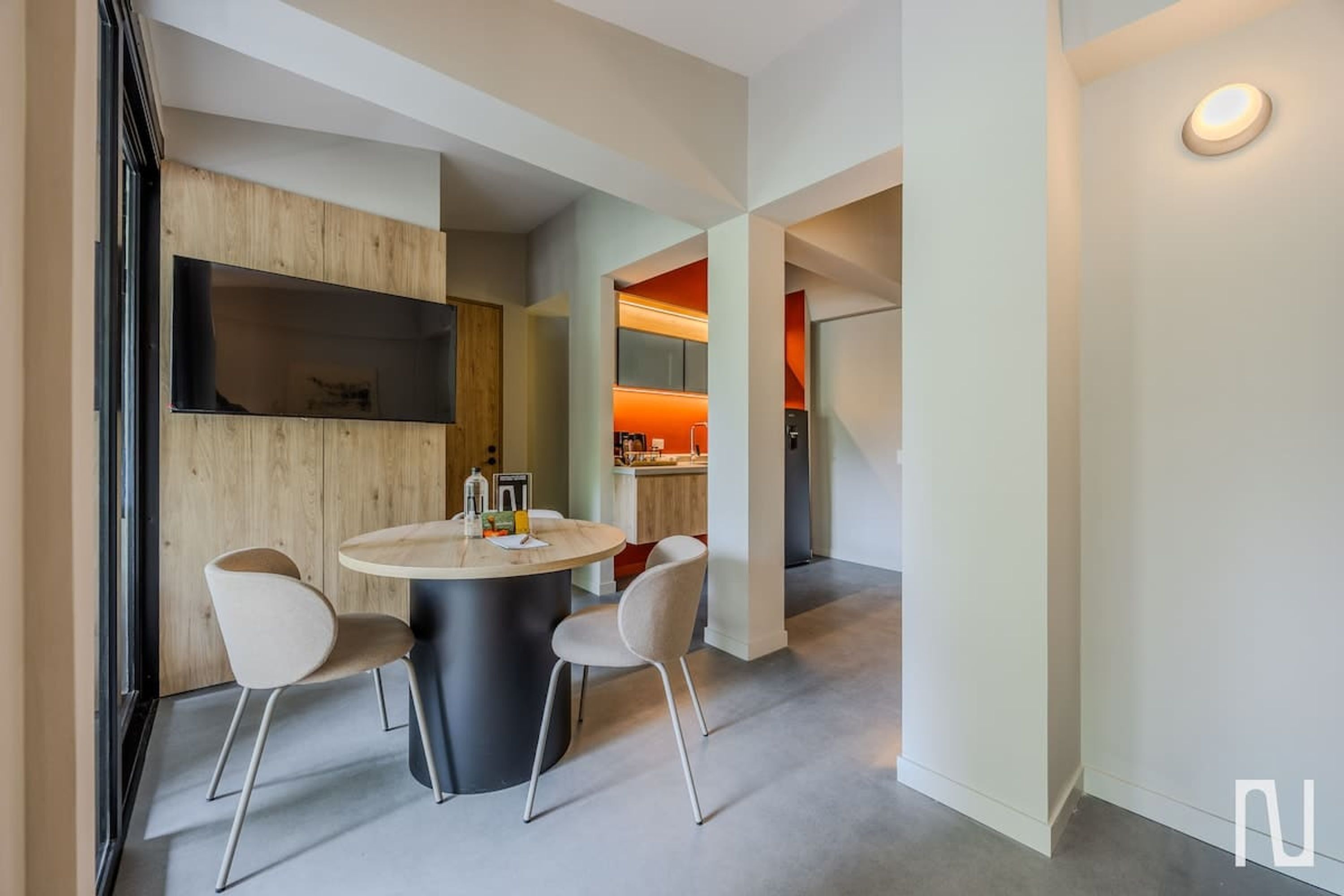 Ein modernes Interieur mit einem runden Esstisch, zwei Stühlen, einer Holzvertäfelung und einer Küche mit roter Beleuchtung.