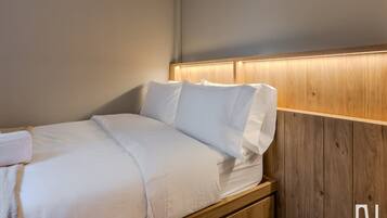Cama bem arrumada com lençóis brancos e cabeceira de madeira.