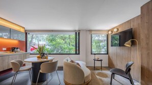 Moderni olohuone, jossa on pyöreä pöytä, kaksi tuolia, sohva, televisio ja pieni sivupöytä.