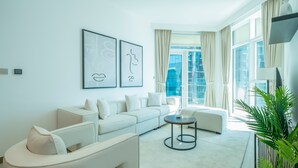 A modern living room with a white sofa, a round coffee table, and a large window with curtains. - Elegant High Floor 2BR Furnished Urban Oasis (Dubai)