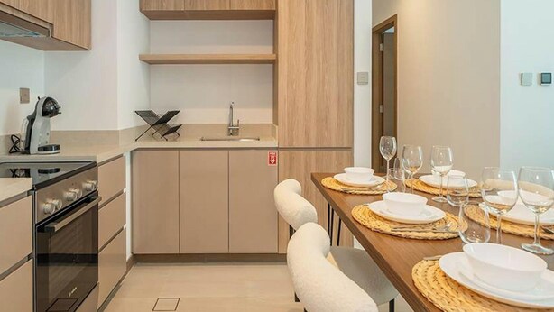 A modern kitchen with wooden cabinets, a built-in oven, and a dining area with a wooden table set for four. - Elegant High Floor 2BR Furnished Urban Oasis (Dubai)