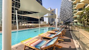 A rooftop pool area with lounge chairs, a swimming pool, and modern buildings in the background. - Elegant High Floor 2BR Furnished Urban Oasis (Dubai)