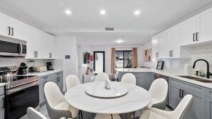 A modern kitchen with white cabinets, a central island with seating, and built-in appliances. - Miami Hotel Home + jacuzzi+sauna +barbecue (Miami)