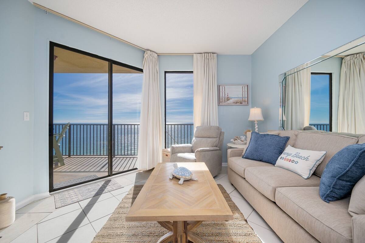 Una sala de estar con un sofá, una mesa de centro, un sillón y vistas al mar a través de amplios ventanales.