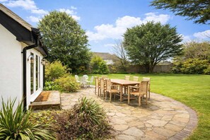 A patio with a stone table and chairs, surrounded by a well-maintained lawn and trees. - Spacious Coastal Family Home, Sleeps 8 (Bognor Regis)