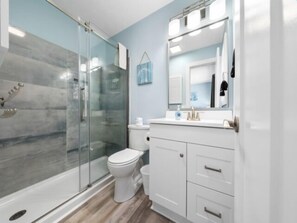 Un baño moderno con cabina de ducha de vidrio, inodoro blanco y tocador con espejo.
