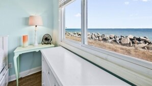 A room with a view of the beach, a white dresser, a lamp, and a small table with a candle. - A Sea Escape 1 Bedroom Villa (Carolina Beach)