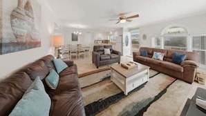 Ein Wohnzimmer mit zwei Sofas, einem Couchtisch und einem Deckenventilator. Im Hintergrund ist ein Essbereich mit Stühlen und einem Tisch zu sehen.