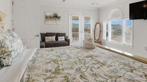 Ein Schlafzimmer mit Bett, Deckenventilator, Kommode, Spiegel und einer Tür, die auf einen Balkon führt.