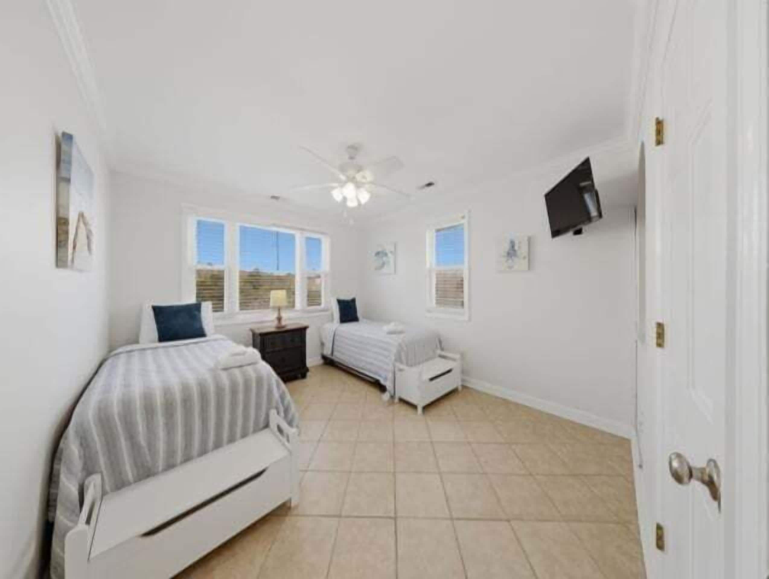 A bedroom with two beds, a desk, a chair, a TV, and a ceiling fan.