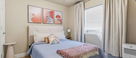 A bedroom with a bed, a ceiling fan, a window with curtains, and artwork on the wall.