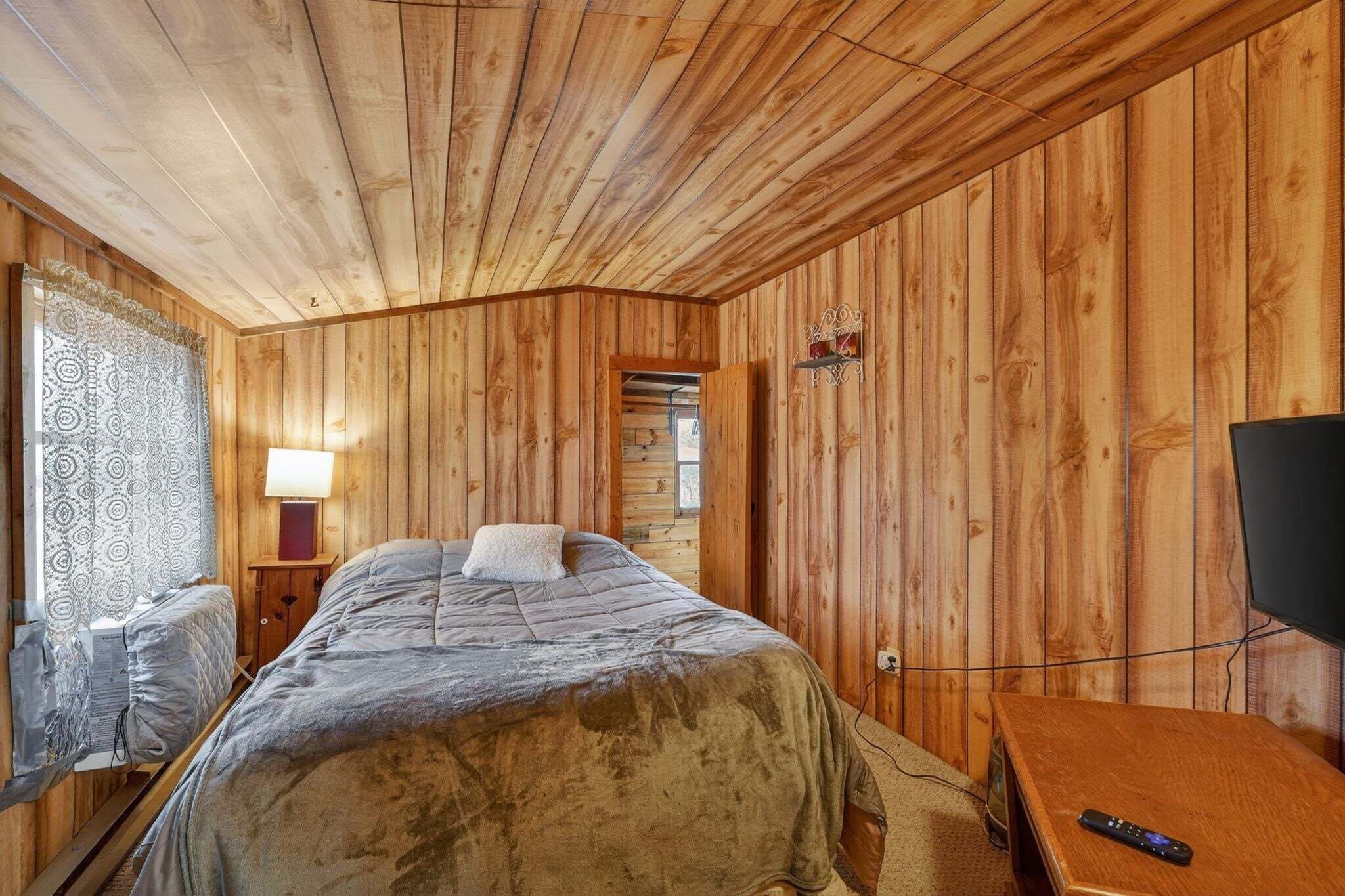 A wooden-paneled room with a bed, a television, and a lamp.