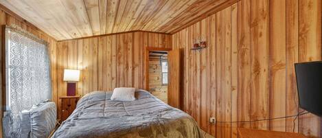 A wooden-paneled room with a bed, a television, and a lamp.
