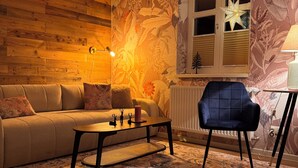 Una sala de estar acogedora con una pared de madera, un mural decorativo, un ventilador de techo, un sofá, una mesa de centro, un sillón azul y un tapete estampado.