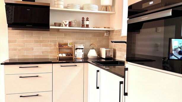 Cocina moderna con armarios blancos, encimera negra y extractor de acero inoxidable.