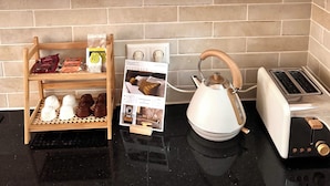Una cocina con platos blancos, una taza con motivos navideños, saleros de madera, una bandeja con copas de chocolate, un hervidor y un tostador.