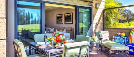 A dining area with a table set for two, a sofa, and a view of a garden.