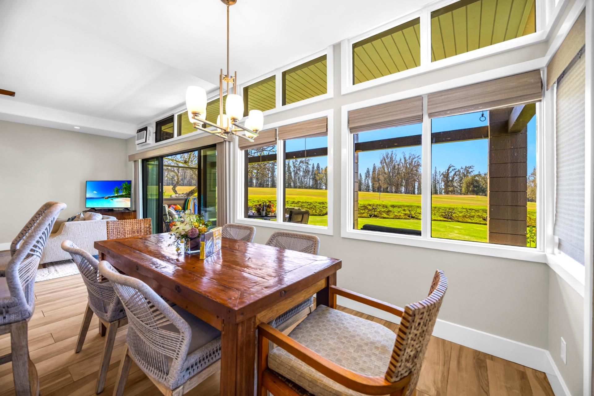 A dining area with a wooden table, wicker chairs, and large windows offering a view of a golf course.