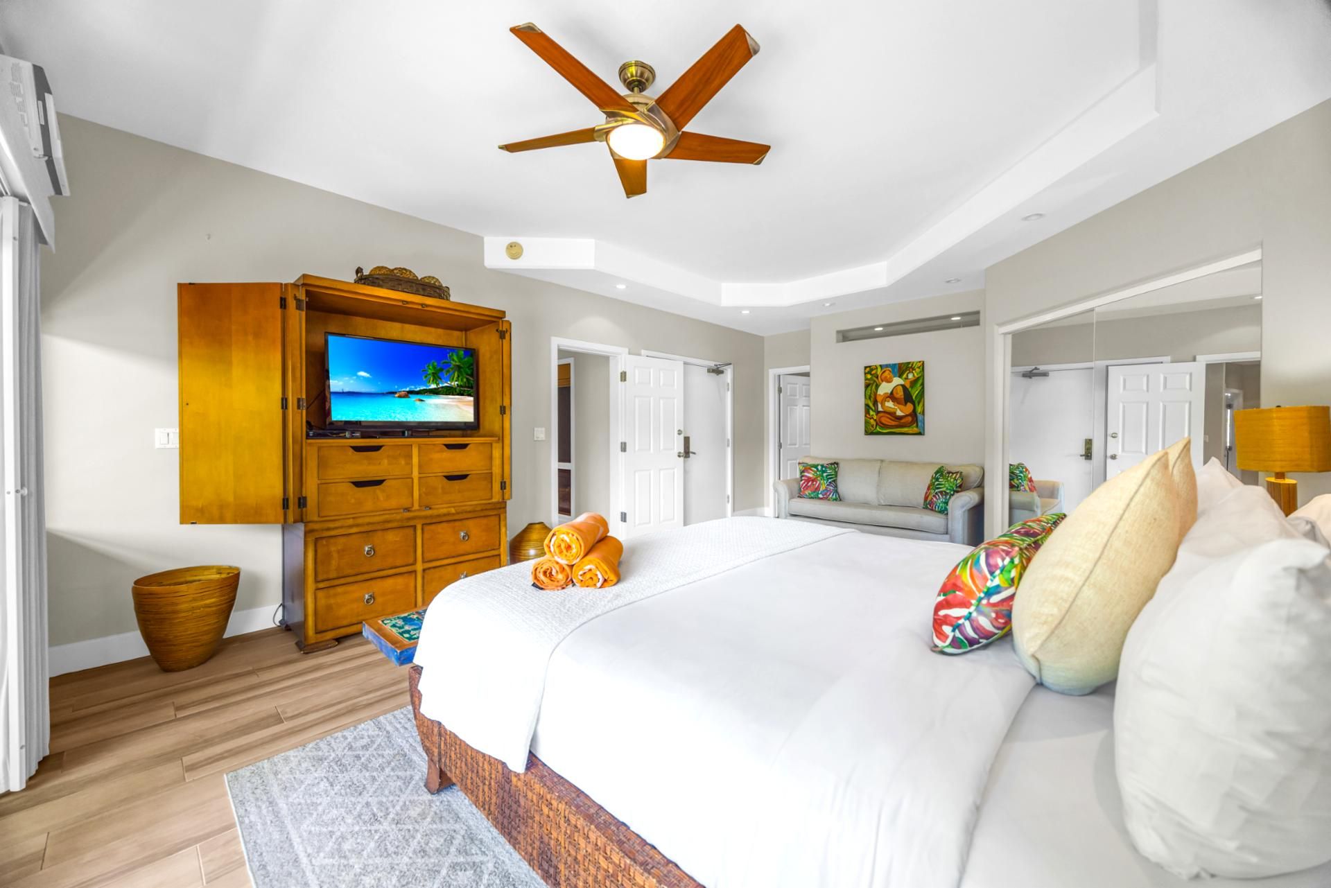 A bedroom with a bed, a ceiling fan, a TV, and a wooden cabinet.
