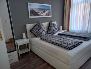 A neatly arranged bedroom with a bed, pillows, a bedside table with a candle, and a framed picture on the wall. - Hotel stückers (Wilster)
