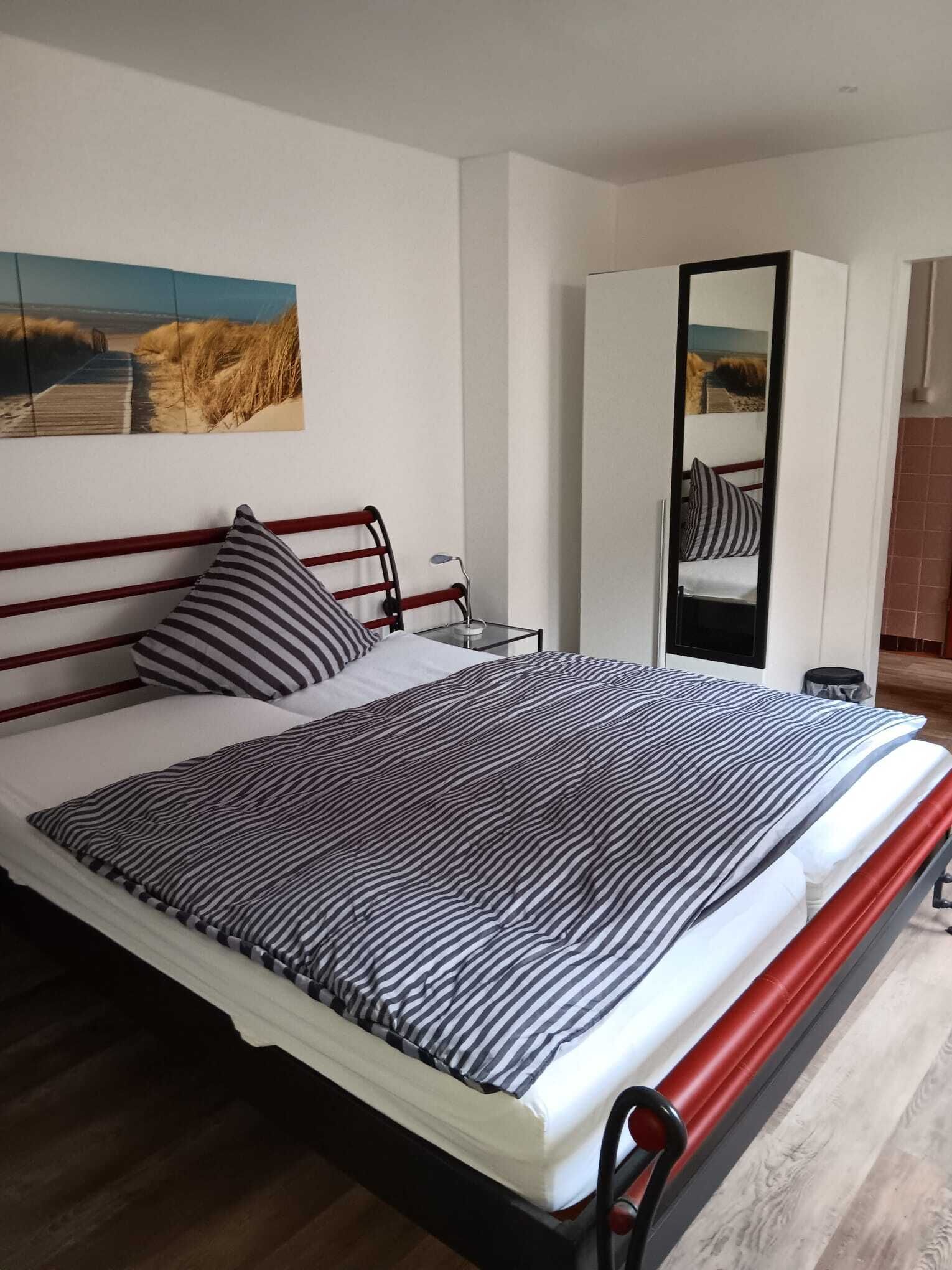 Una cama con una colcha a rayas, una mesita de noche con una lámpara, un espejo y un cuadro en la pared.