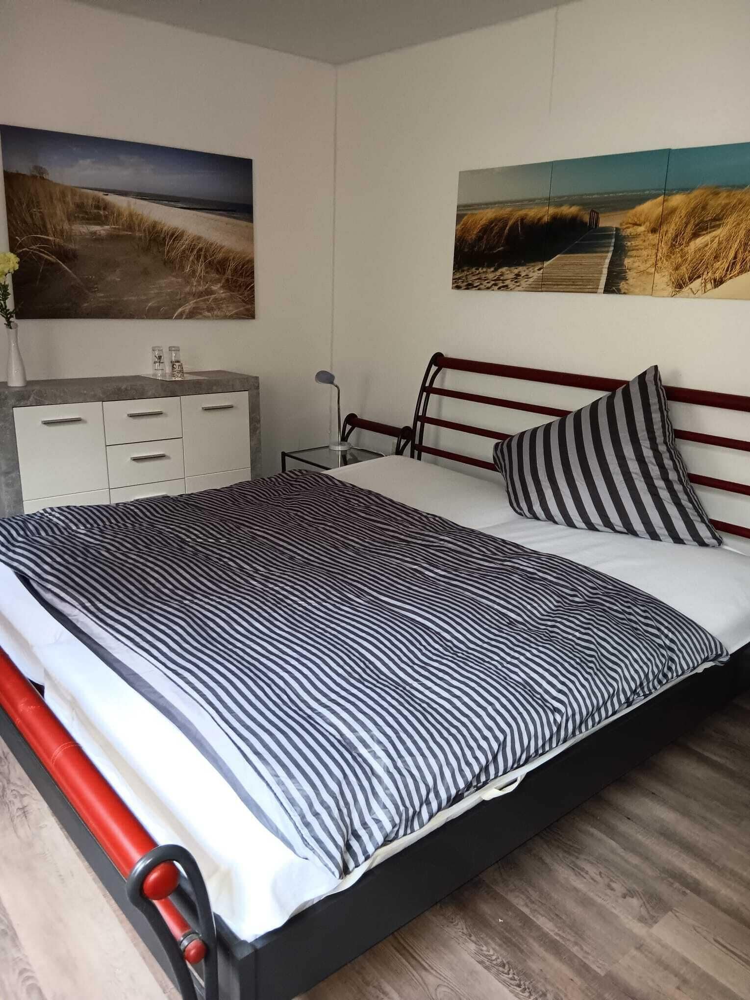 Een slaapkamer met een bed, een nachtkastje, een dressoir en twee landschapsschilderijen aan de muur.