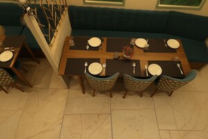 Un comedor con una mesa de madera dispuesta para cuatro personas, rodeada de sillas de mimbre y un sofá azul aguamarina al fondo.