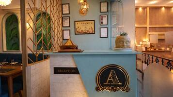 A reception area with a blue counter, a 'RECEPTION' sign, framed certificates, and a Buddha statue.