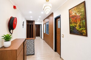 Un pasillo con piso de madera, una planta en maceta, un hidrante rojo, un candelabro y un cuadro en la pared.