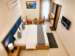 A hotel room with a bed, bedside table, lamp, TV, and a painting on the wall. - Andies Hotel (Kharar)
