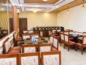 A dining area with multiple tables and chairs, a buffet setup with food containers, and a chandelier. - Andies Hotel (Kharar)