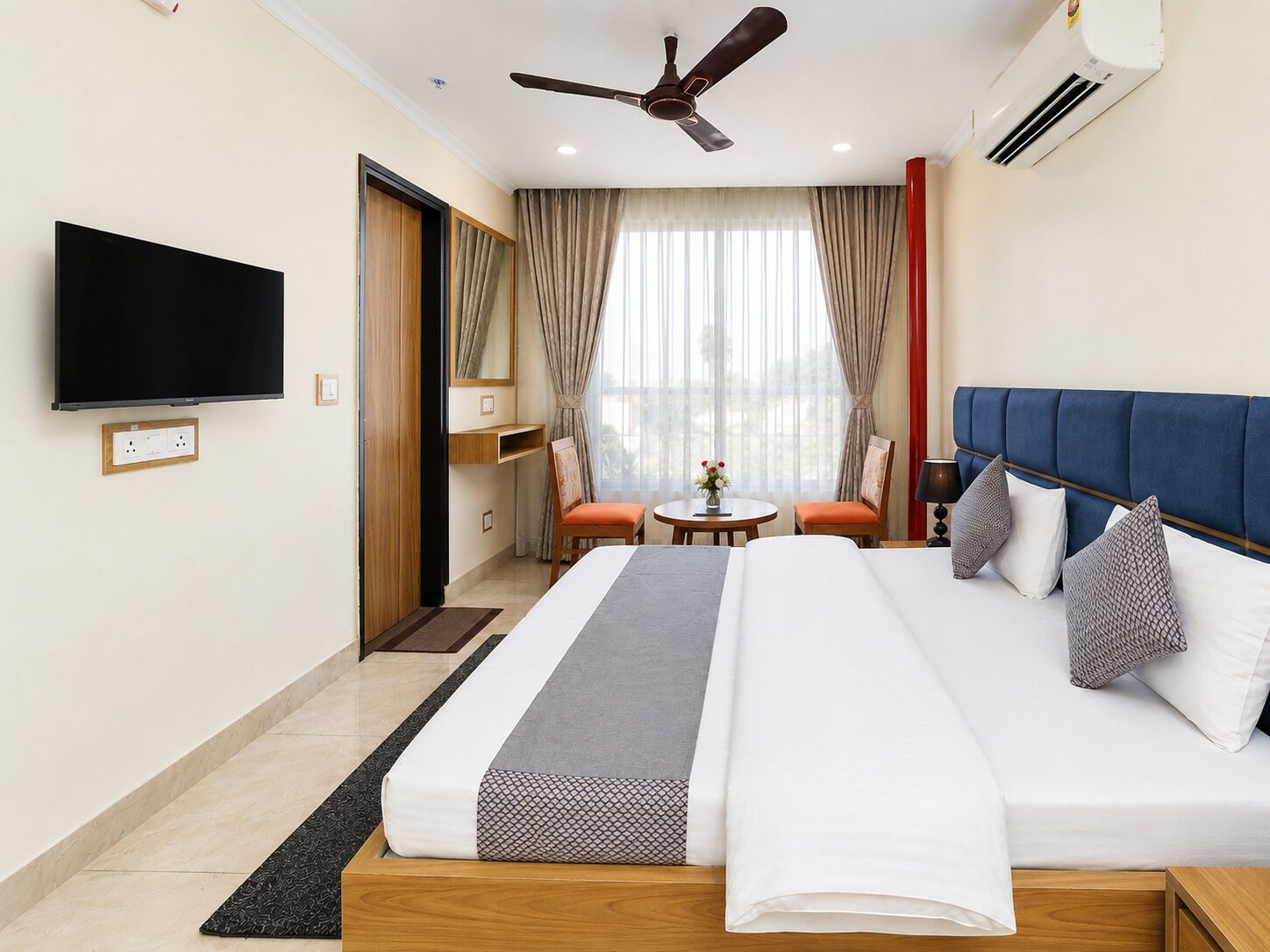 Habitación de hotel con cama, televisor, ventilador de techo y aire acondicionado.