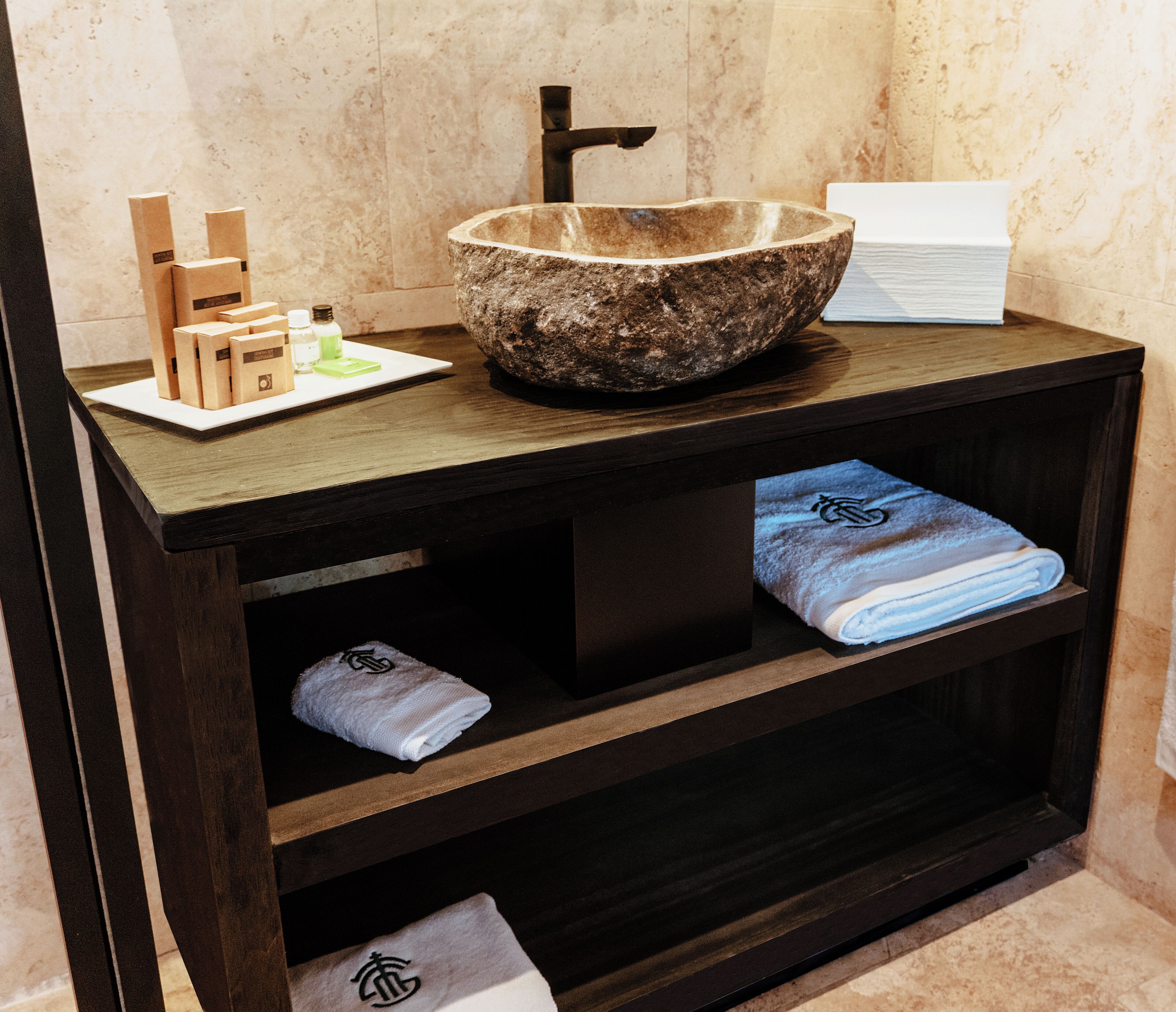 Un lavamanos de baño con un lavabo de piedra, armarios de madera y toallas dobladas con cuidado.
