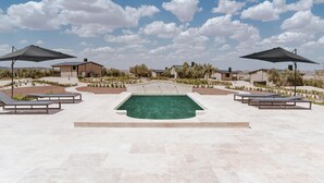 A pool area with lounge chairs and umbrellas, surrounded by stone buildings and greenery. - FINCA LOS COLLADOS DE SAN MIGUEL (Villamanrique)