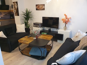 A modern living room with a sofa, a coffee table, a TV, a plant, and a vase with flowers.