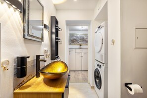 Une salle de bain moderne avec un grand lavabo en forme de cuvette, un miroir, un distributeur de serviettes et un lave-linge.