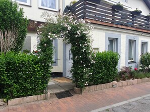 A residential building with a white facade, a wooden balcony, and a rose-covered archway at the entrance. - Apartment 'Hochwertige' with Wi-Fi (Lübeck)