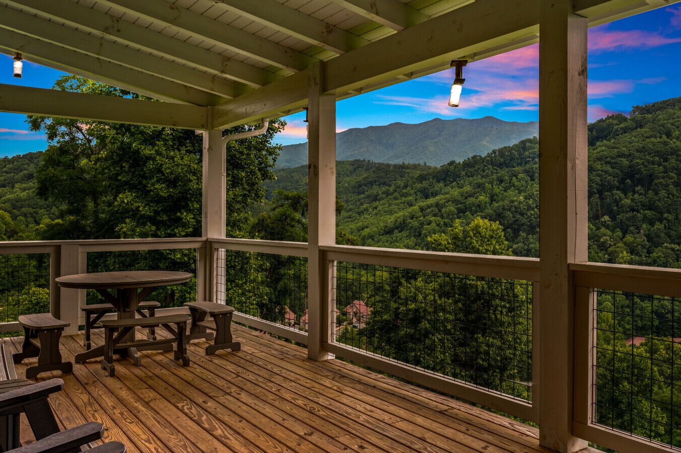 A wooden deck with picnic tables and a view of a forested mountain range.