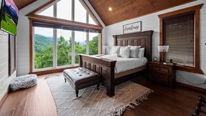 A bedroom with a large window, a bed with a headboard, a nightstand, and a view of the outdoors. - Gatlinburg Splash-Home Theater-Heated Indoor Pool-Game Room! (Gatlinburg)