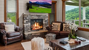 A cozy living room with a stone fireplace, leather furniture, and a large TV mounted above it. - Gatlinburg Splash-Home Theater-Heated Indoor Pool-Game Room! (Gatlinburg)