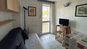 Un soggiorno con divano, televisore su mobile in legno, termosifone, finestra con tende e porta che dà sull'esterno.
